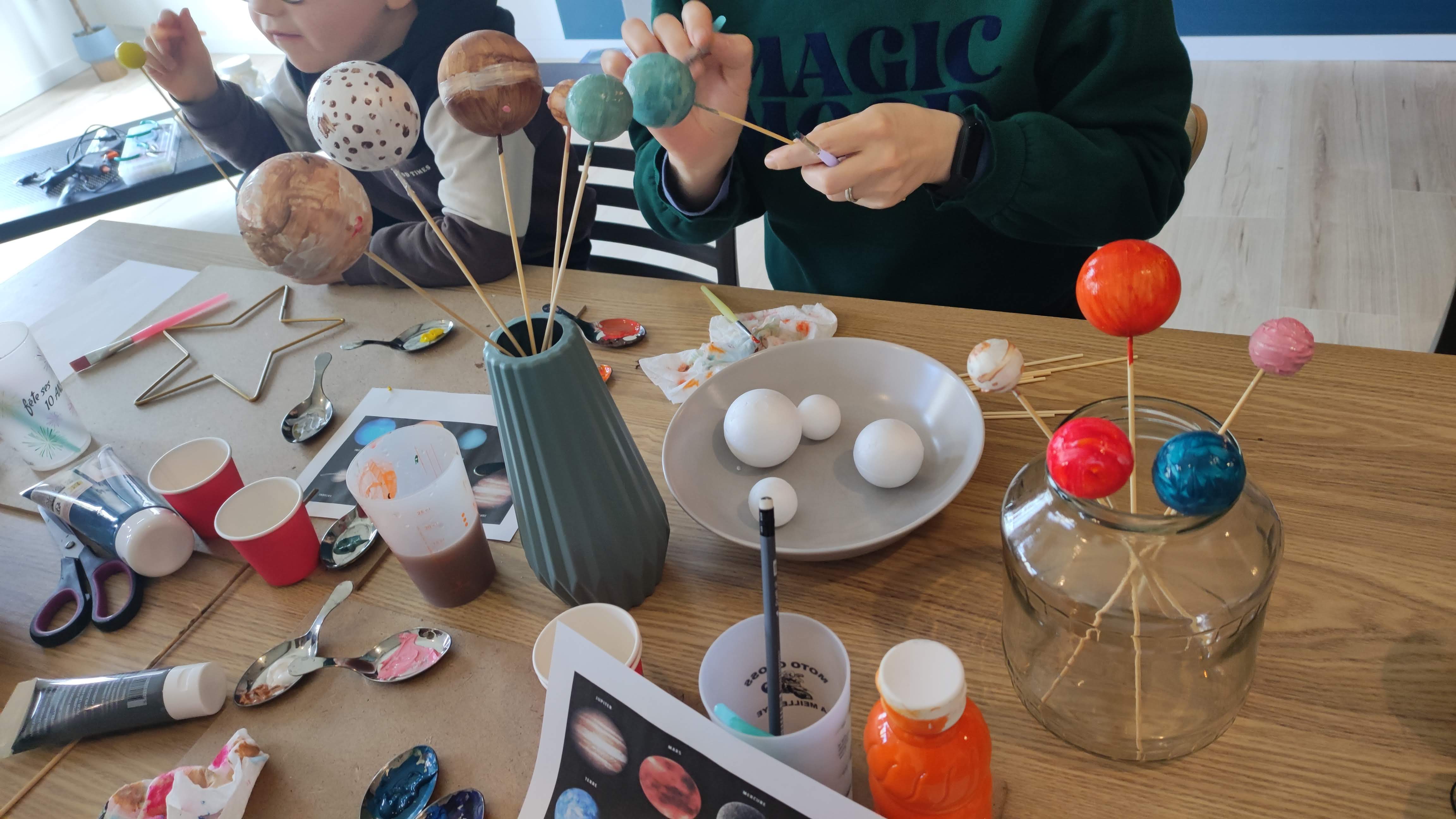Un enfant et un parent créent des planètes lors d’un goûter créatif Sous le Pommier